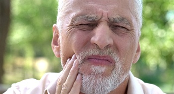 An older man holds his mouth while experience pain caused by a failed dental implant in Daytona Beach