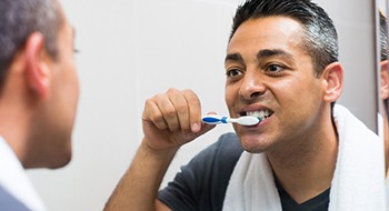 A man uses a manual toothbrush to clean his teeth after receiving dental implants in Daytona Beach