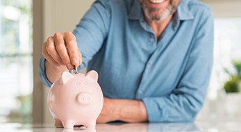 smiling man putting coins into a pink piggy bank 