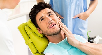 Grimacing man in dental chair holding jaw