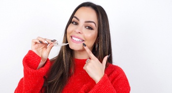 Patient pointing to her smiling while holding her clear aligners