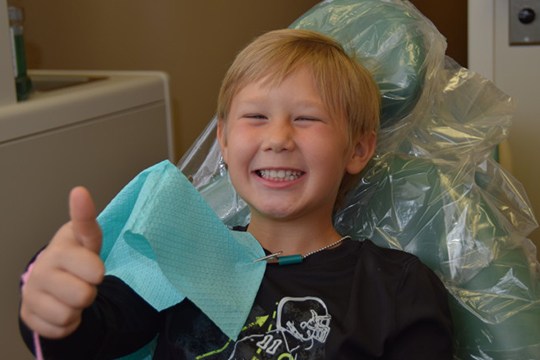 Young boy in dental chair giving thumbs up