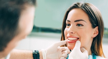 cosmetic dentist examining female patient’s teeth during consultation