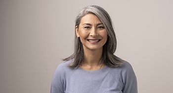 Mujer en camisa gris sonriendo mientras mira a la cámara