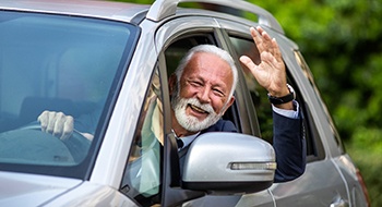 a person smiling and waving from their car window