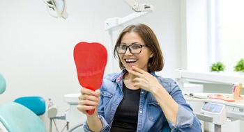 A middle-aged woman admires her restored smile after suffering from dental implant failure in Daytona Beach