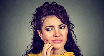 A young female wearing a yellow blouse is holding her mouth in pain because of dental implant failure in Daytona Beach