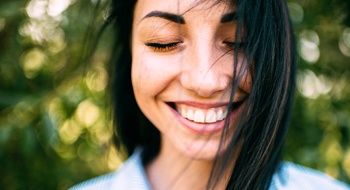 person in a park smiling with their eyes closed