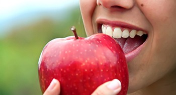 Person with dental implants in Daytona Beach eating an apple.