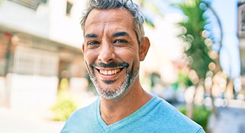 A middle-aged man wearing a blue shirt smiles after learning proper dental implant care in Daytona Beach