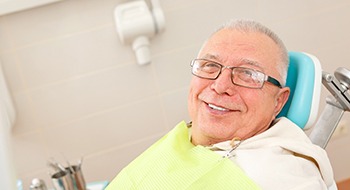 An older man with glasses smiles in preparation for a dental checkup after receiving dental implants in Daytona Beach