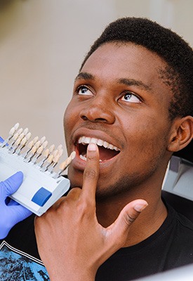 Man in dental chair pointing to teeth with shade guide held up
