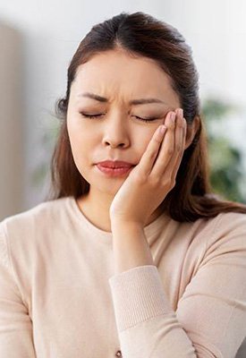 Woman in tan sweater holding hand to face in pain