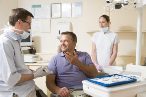 Dentist and assistant in exam room with man in chair smiling