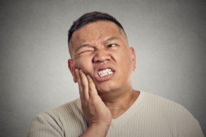 Pained man hand on cheek wonders what constitutes a dental emergency